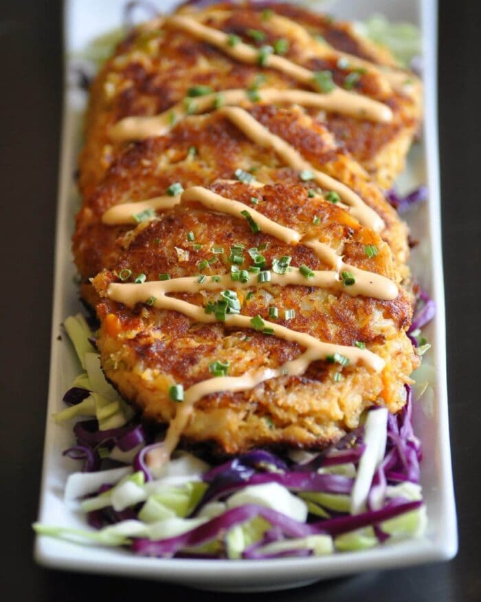 Cajun crab cakes topped with remoulade lined on a square platter 