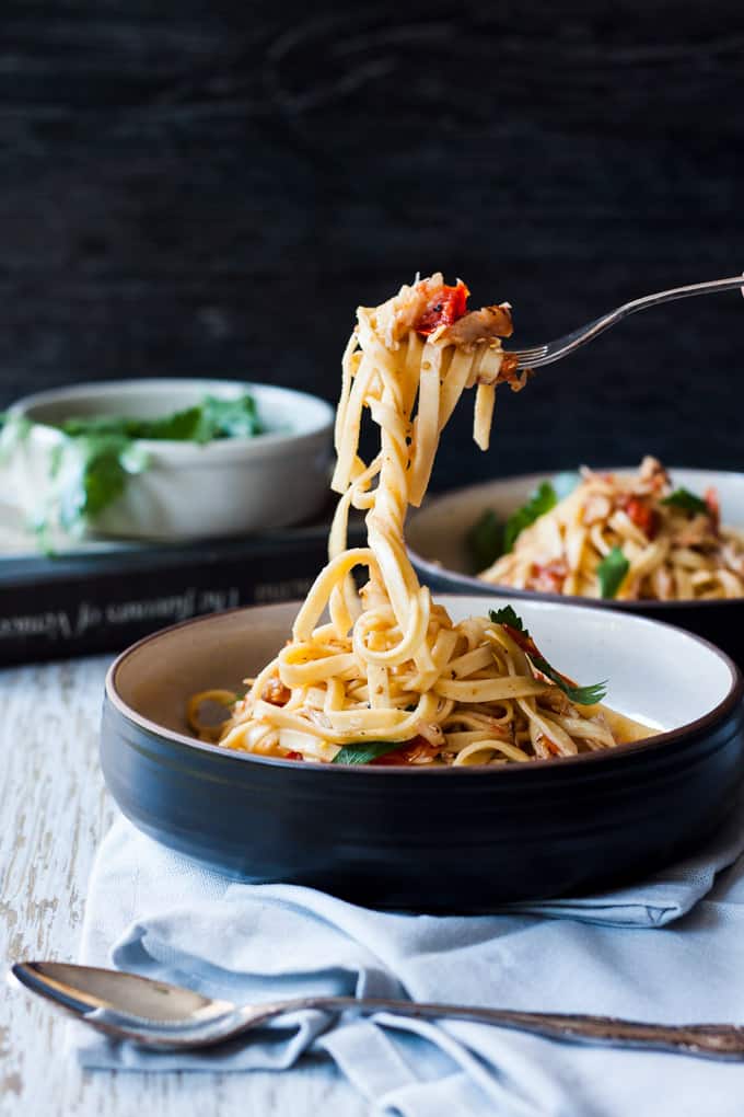 Venetian crab linguine in a dark bowl with a white interior, being lifted in the air on a fork