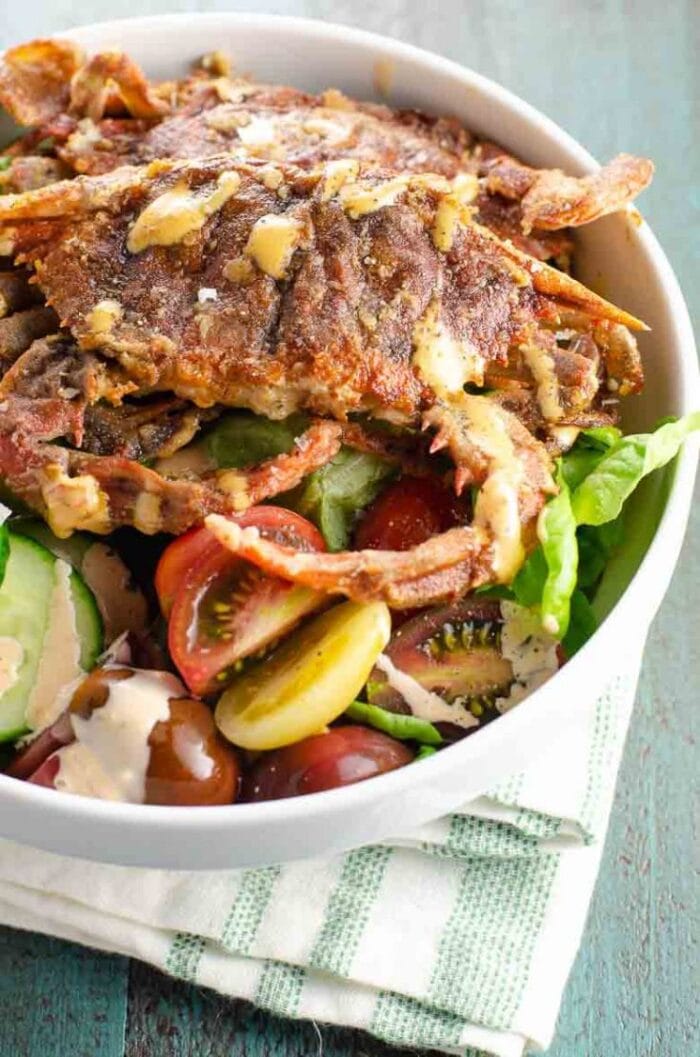 Fried soft shell crab on a salad in a large white bowl