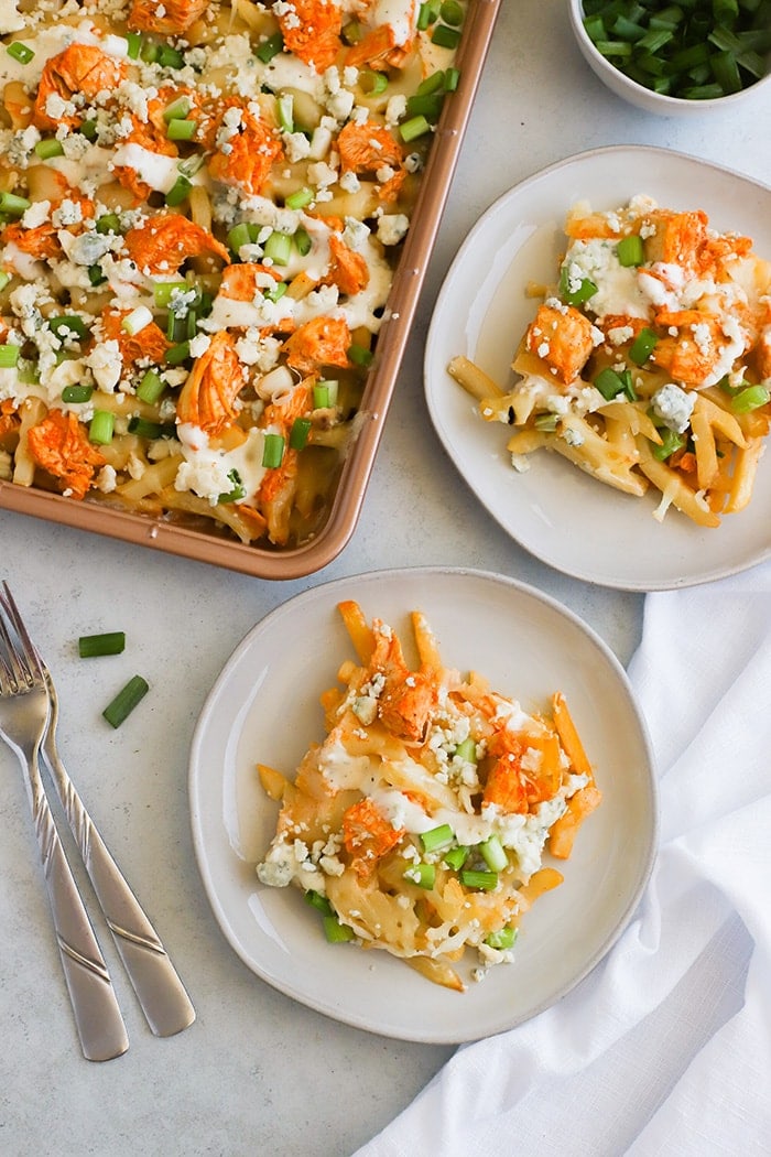 Two plates of shredded chicken nacho fries next to a large pan of fries