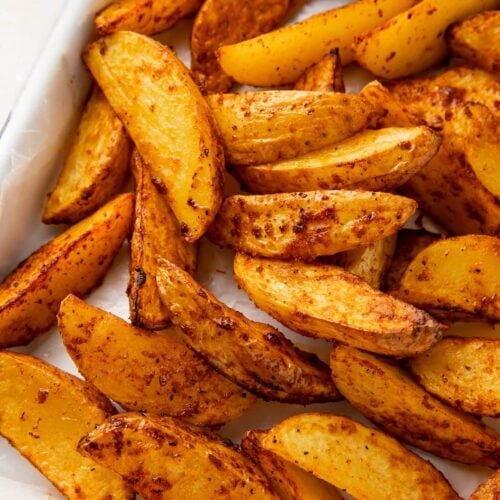 Air fryer potato wedges on a sheet pan next to a ramekin of ketchup