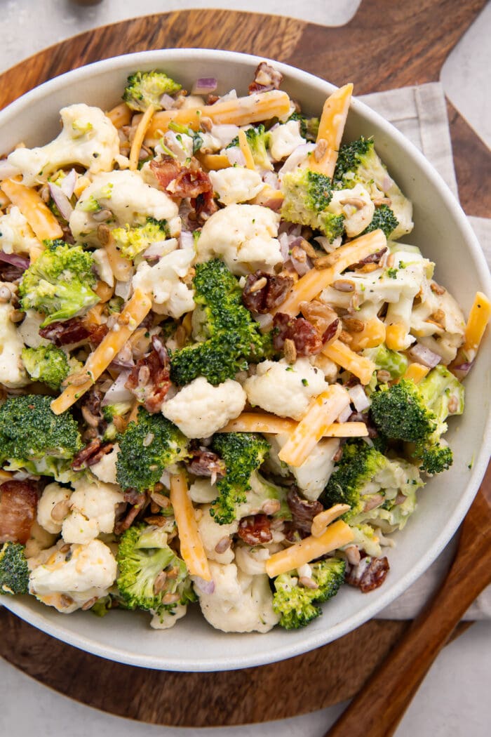 A bowl of broccoli cauliflower salad on a wooden cutting board