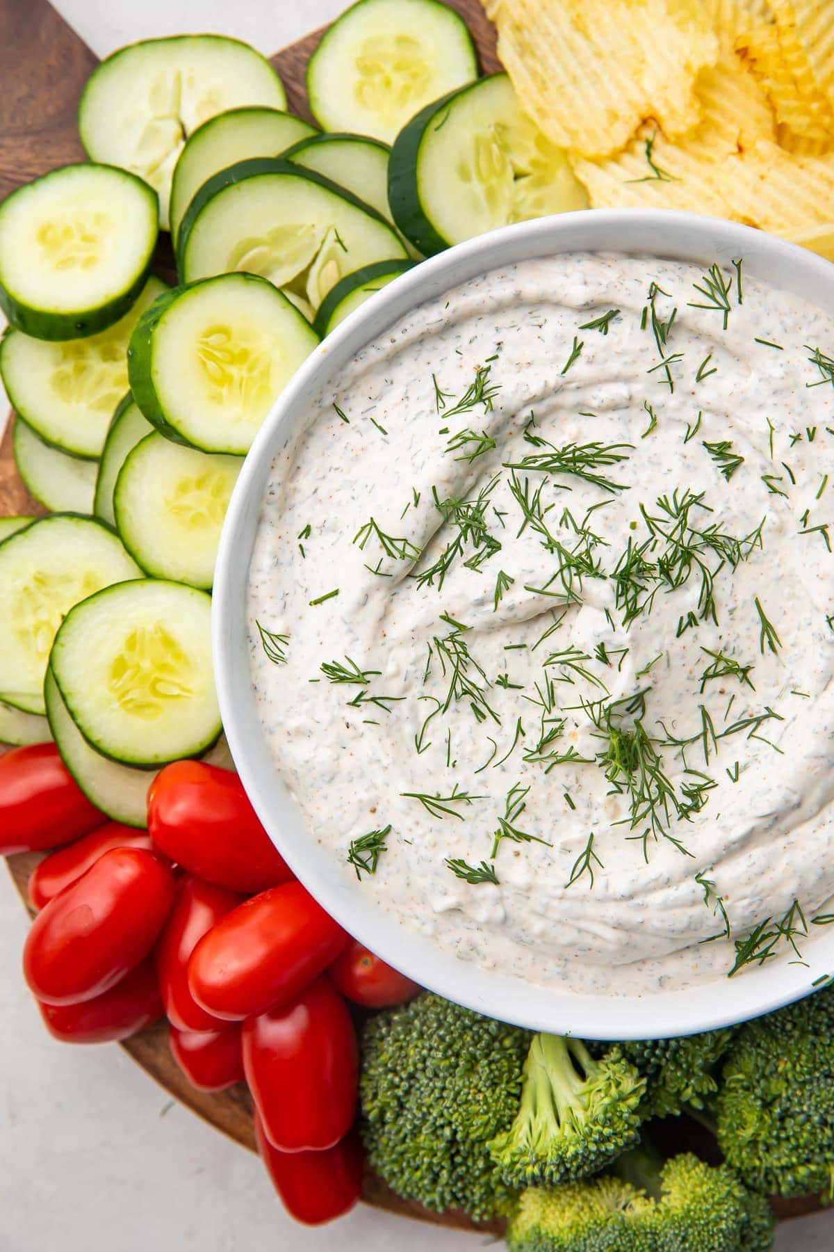 A bowl of dill dip surrounded by veggies