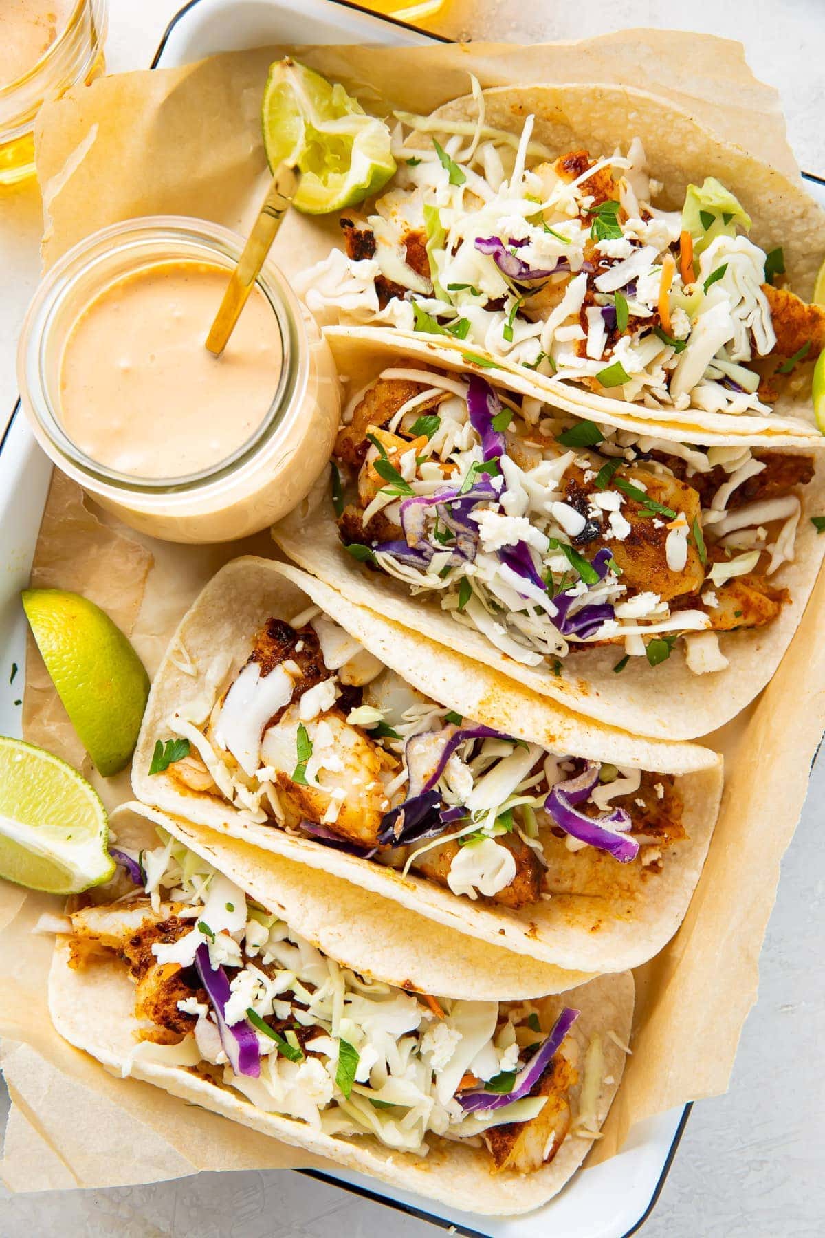 4 fish tacos lined up on a platter next to a glass jar of fish taco sauce