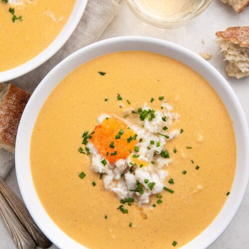 Overhead view of a white bowl of she crab soup with a glass of water at the top of the photo