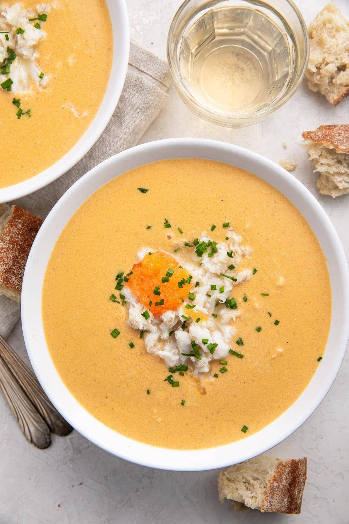 Overhead view of a white bowl of she crab soup with a glass of water at the top of the photo