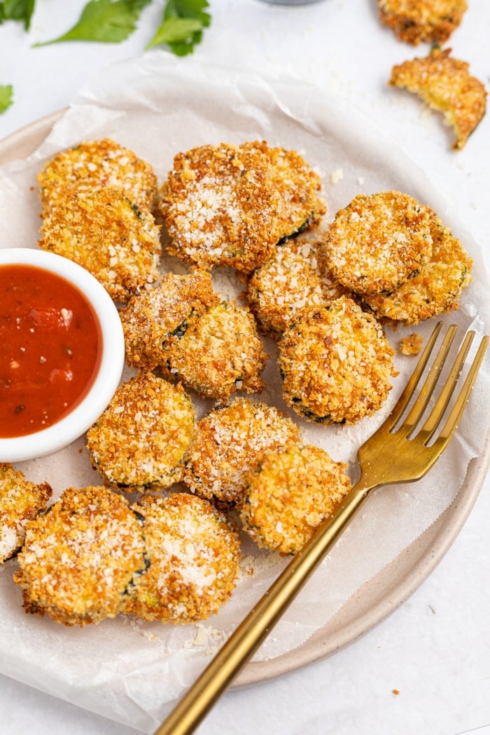 Air Fryer Zucchini Chips on a plate, sprinkled with parmesan cheese and served with marinara sauce.