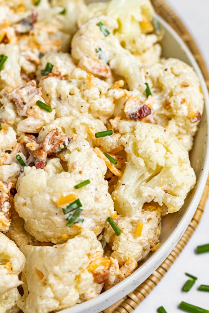 Cauliflower salad in a bowl with chives sprinkled on and around the bowl.