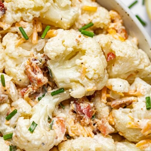 Close up image of cauliflower salad in a bowl with chives sprinkled on top and a lemon on the side.