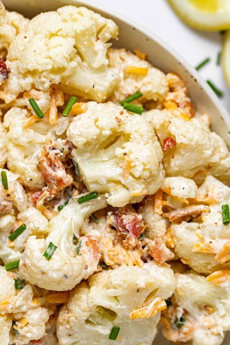 Close up image of cauliflower salad in a bowl with chives sprinkled on top and a lemon on the side.