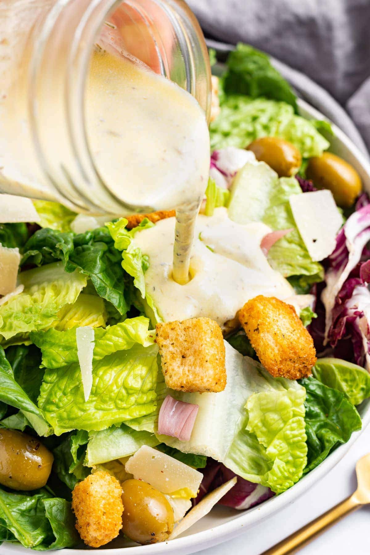 Creamy Italian dressing being poured over a salad with croutons and parmesan cheese.