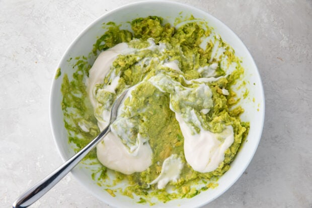 Ingredients for guacamole dip in bowl with spoon