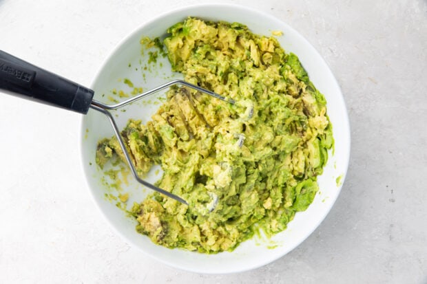 Mashed avocado in bowl with potato masher