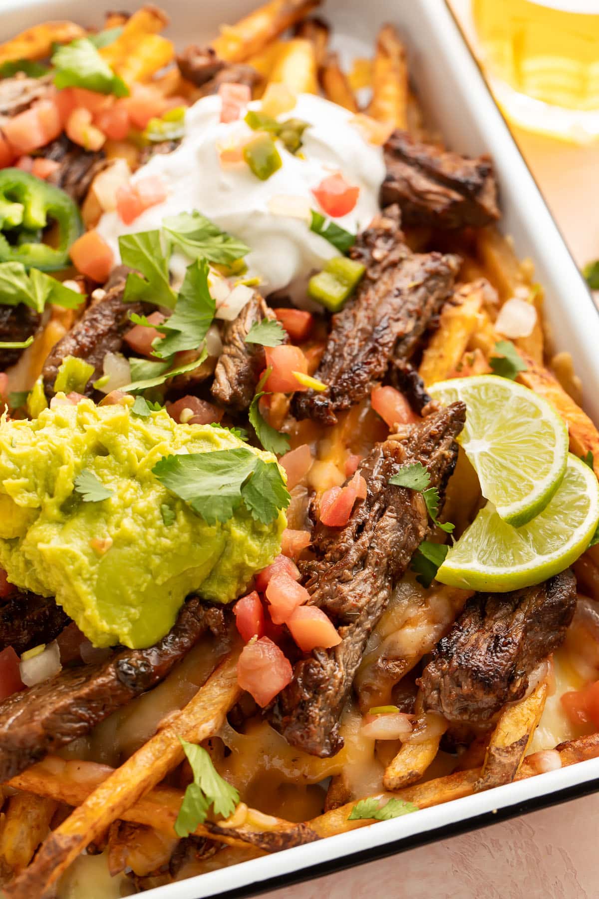 A sheet pan of loaded carne asada fries topped with guacamole, sour cream, cheese, and green onions.