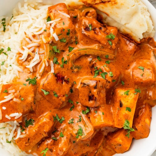 Deep orange paneer tikka masala in a white bowl with white rice and a piece of naan.