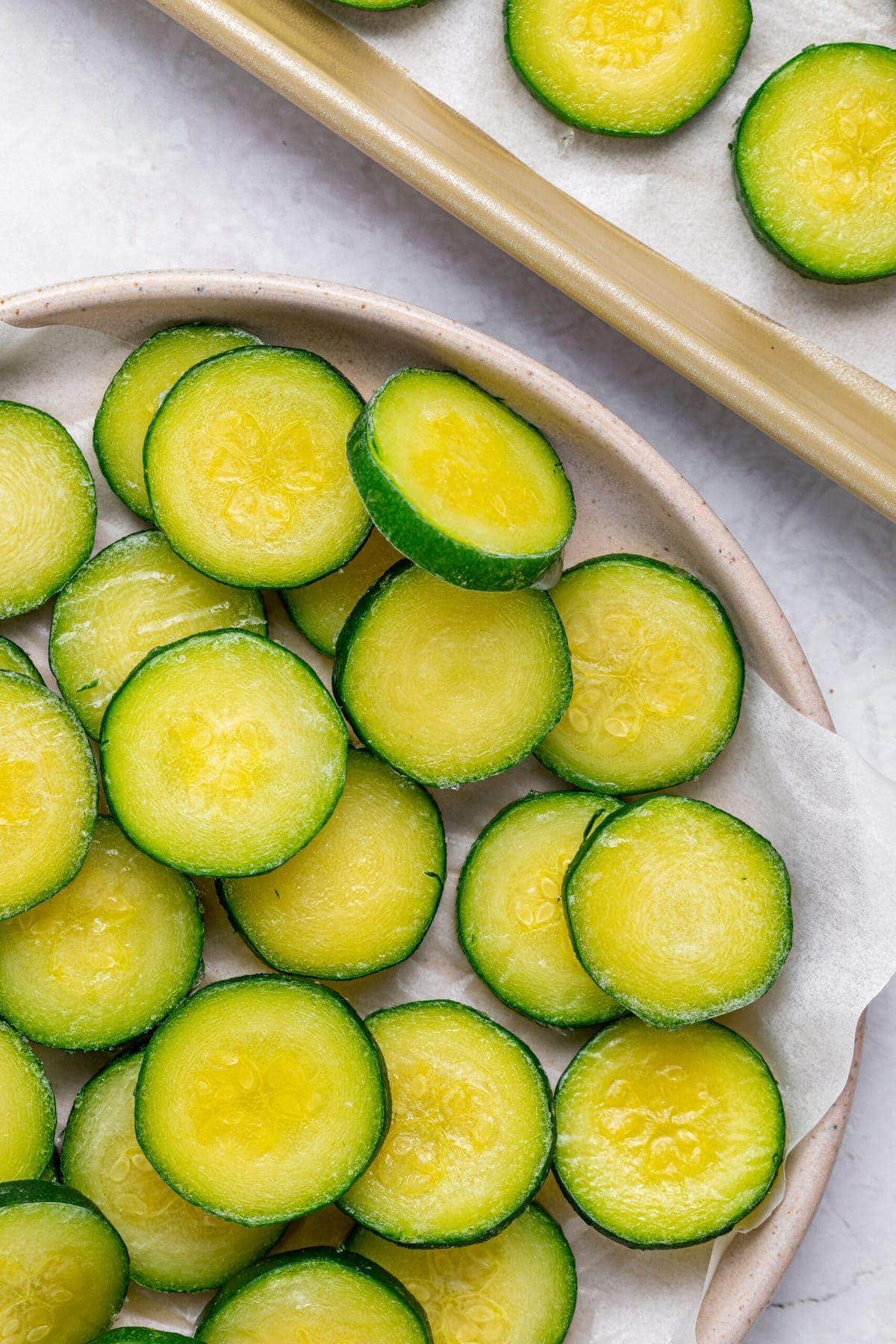 frozen sliced zucchini on a plate and on a baking tray