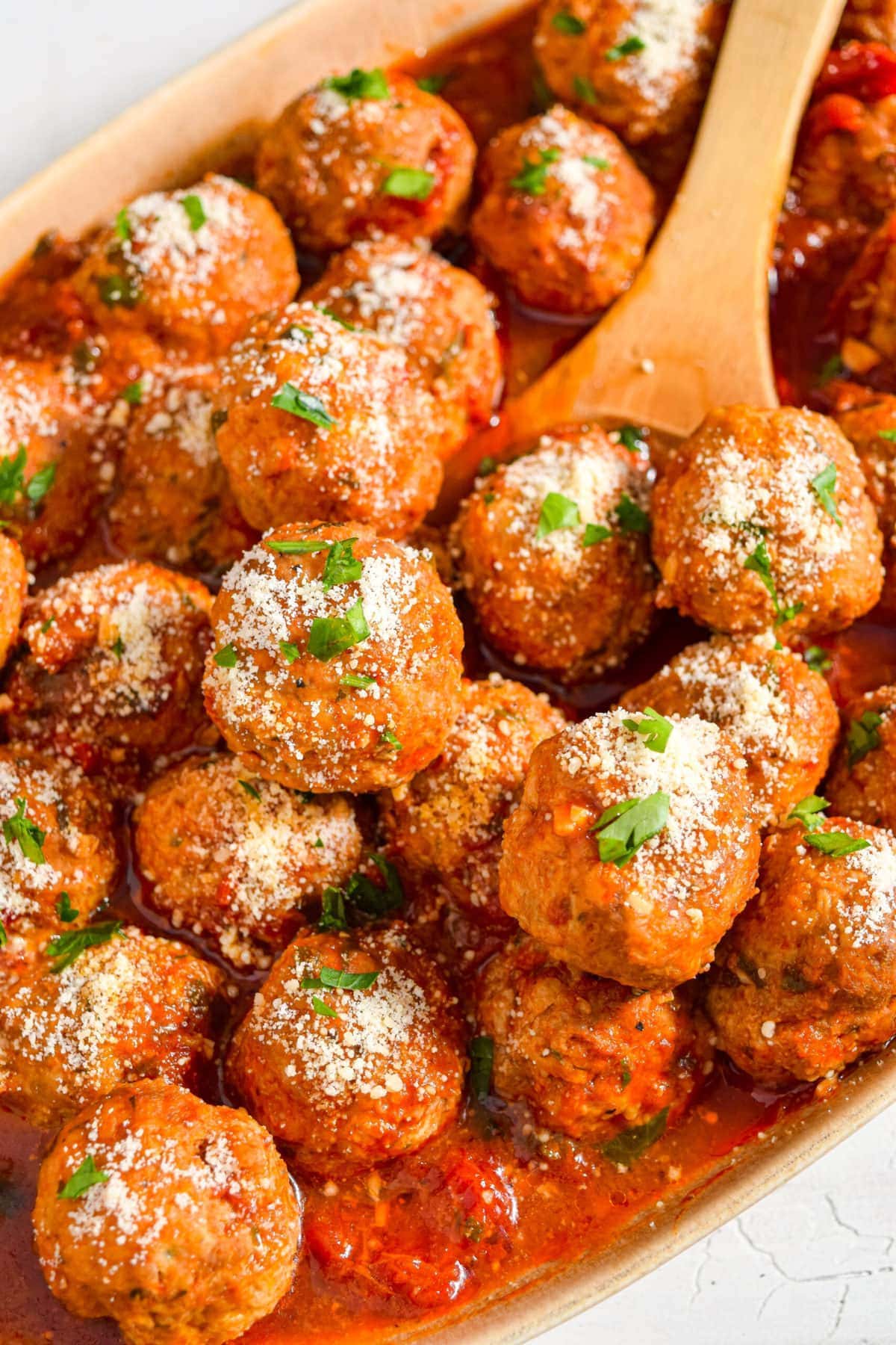 Close up image of instant pot meatballs in a serving dish with a wooden spoon.