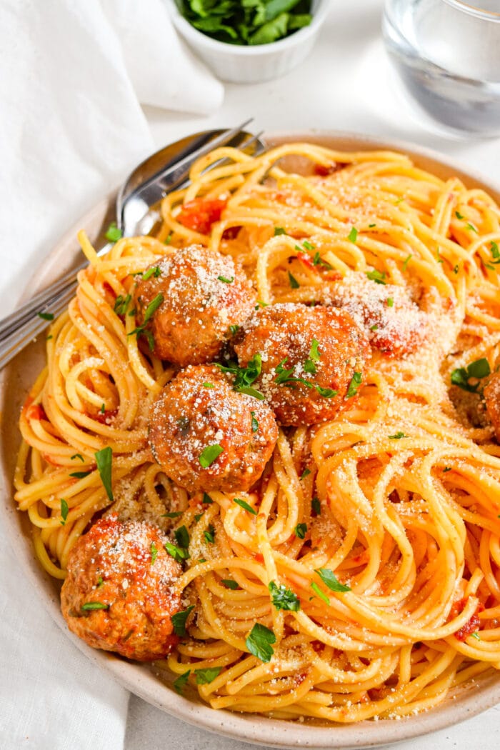 Instant pot meatballs served over spaghetti with a side of fresh parsley.