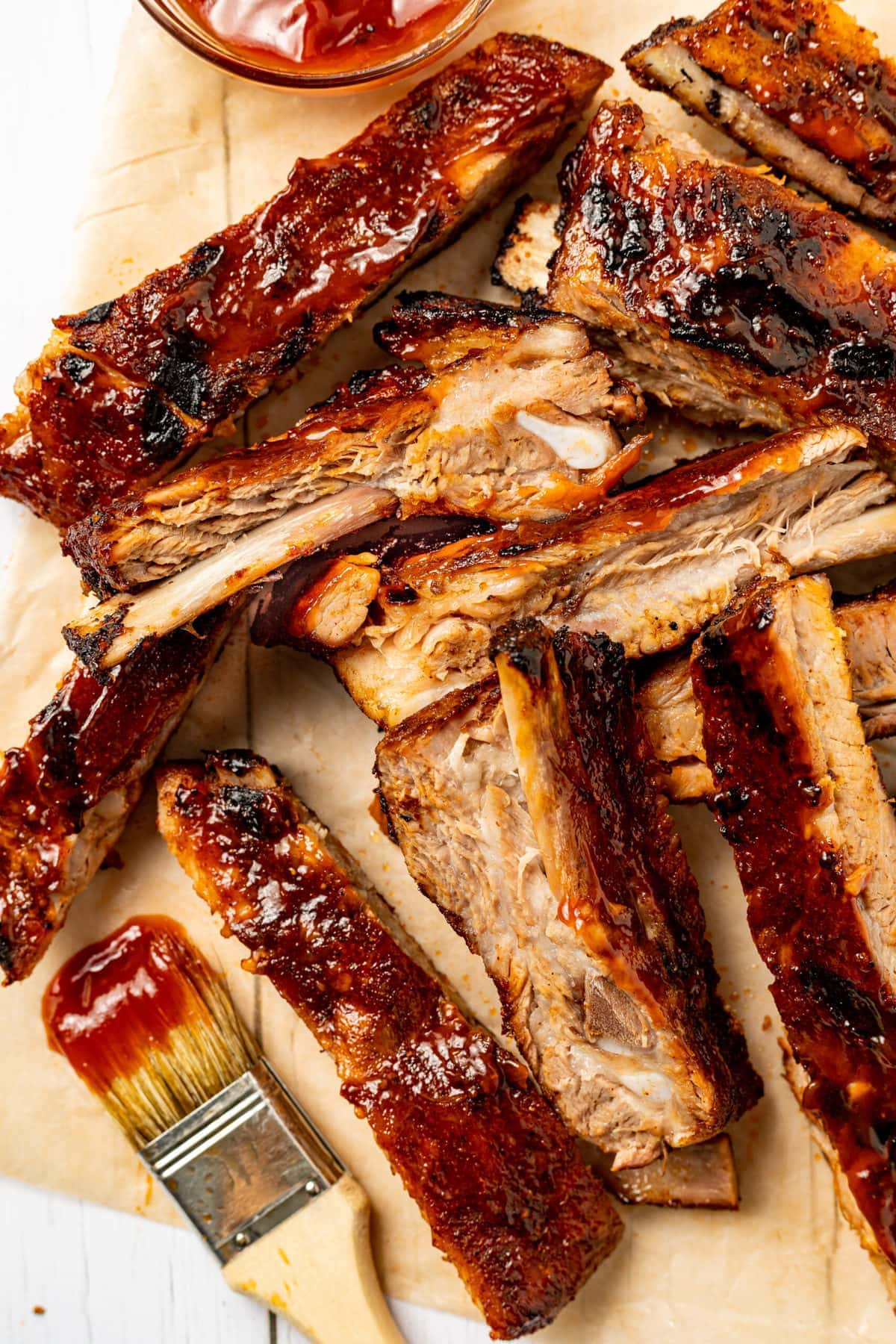 Sliced ribs on a sheet of parchment paper with a side of barbecue sauce.