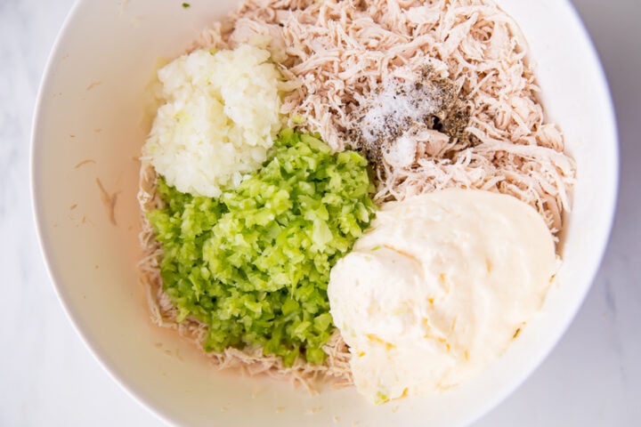 Ingredients for keto chicken salad in a large mixing bowl on a neutral background.