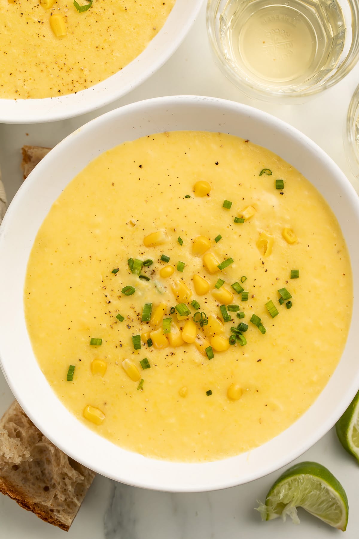 A white soup bowl holding a thick, creamy yellow corn soup topped with corn kernels and chopped green onions.