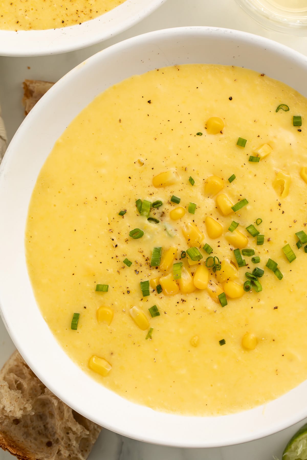 A white soup bowl holding a thick, creamy yellow corn soup topped with corn kernels and chopped green onions.