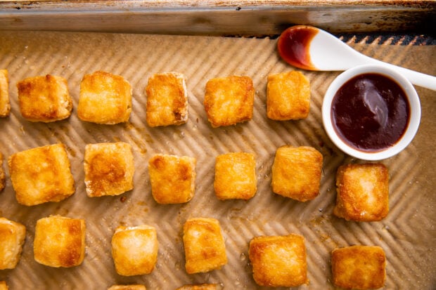 Crispy baked tofu on a baking sheet next to a small bowl of marinade