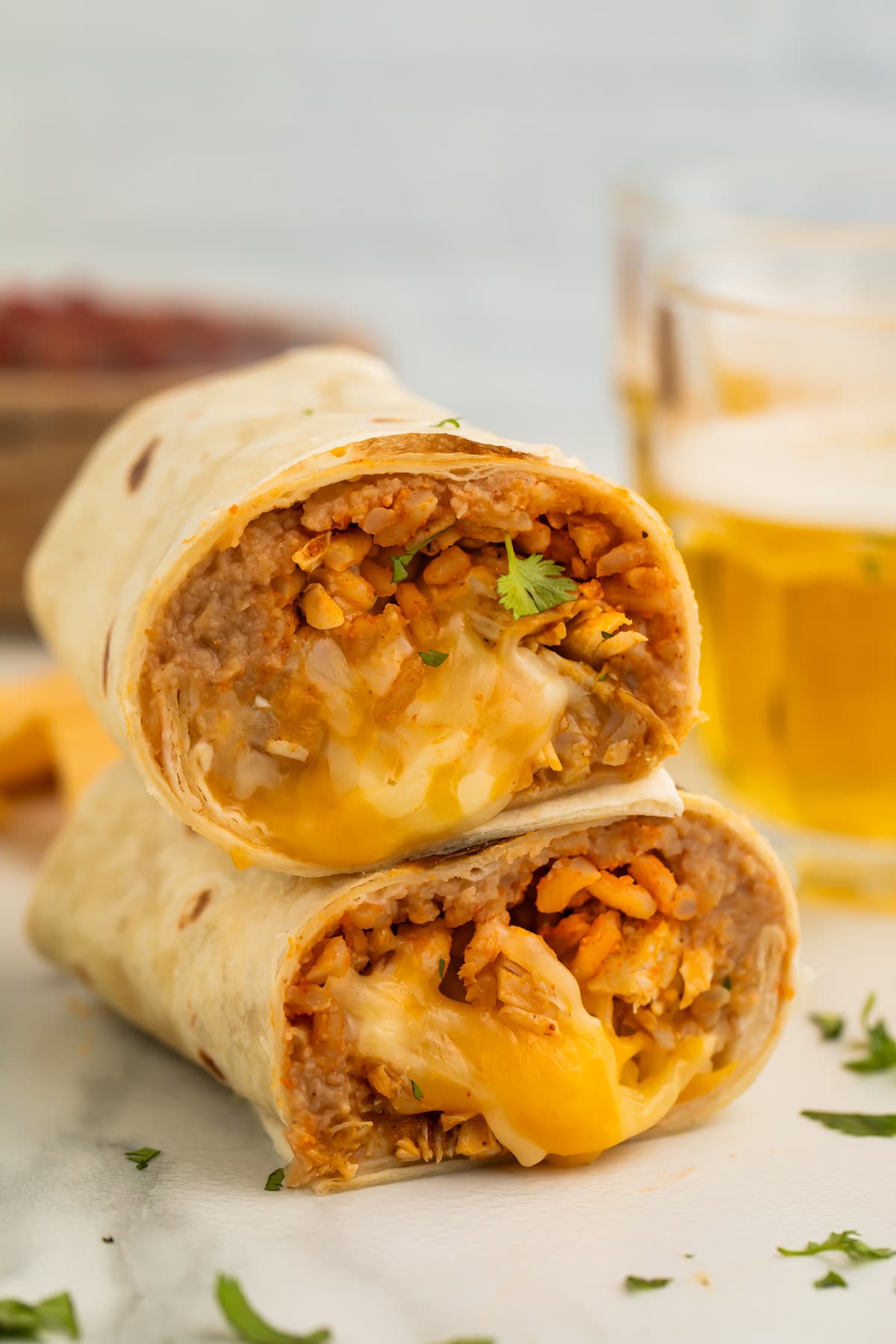 Two halves of a chicken burrito stacked on top of each other, showing a filling of chicken, rice, beans, and gooey cheese.