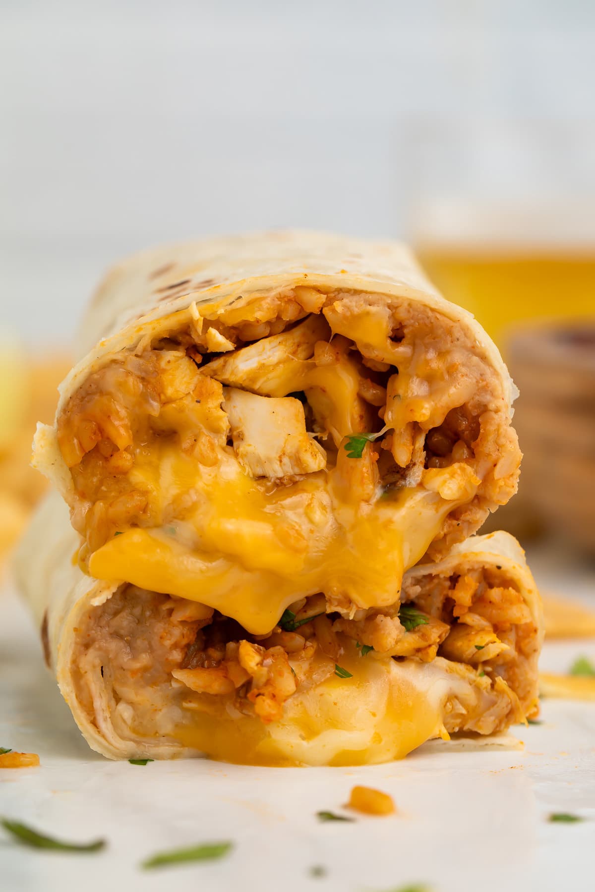 Two halves of a chicken burrito stacked on top of each other, showing a filling of chicken, rice, beans, and gooey cheese.