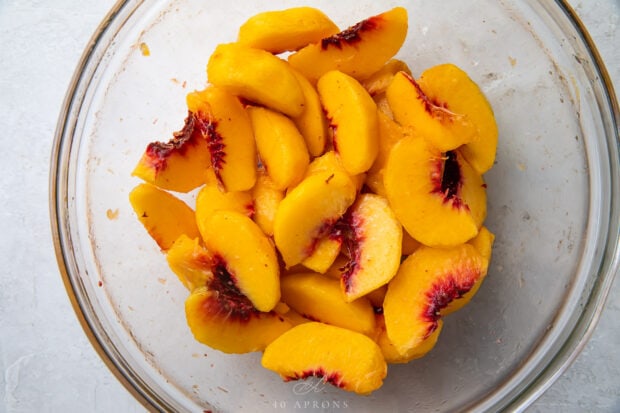 Peach slices in a glass mixing bowl with lemon juice