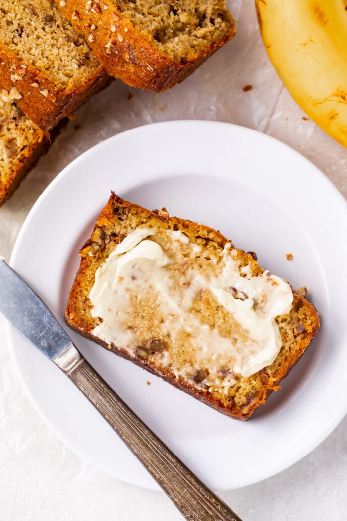 A slice of keto banana bread with butter on a white plate with a butter knife