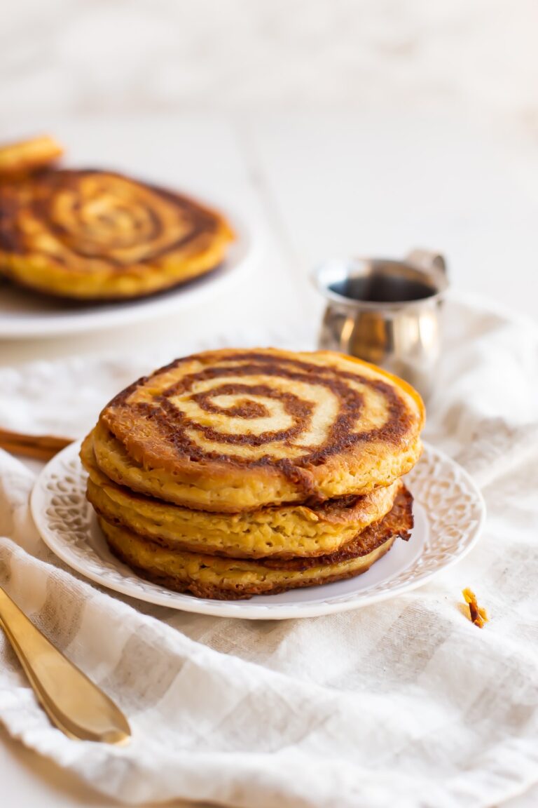 A stack of paleo cinnamon roll pancakes on a white plate on a white tablecloth