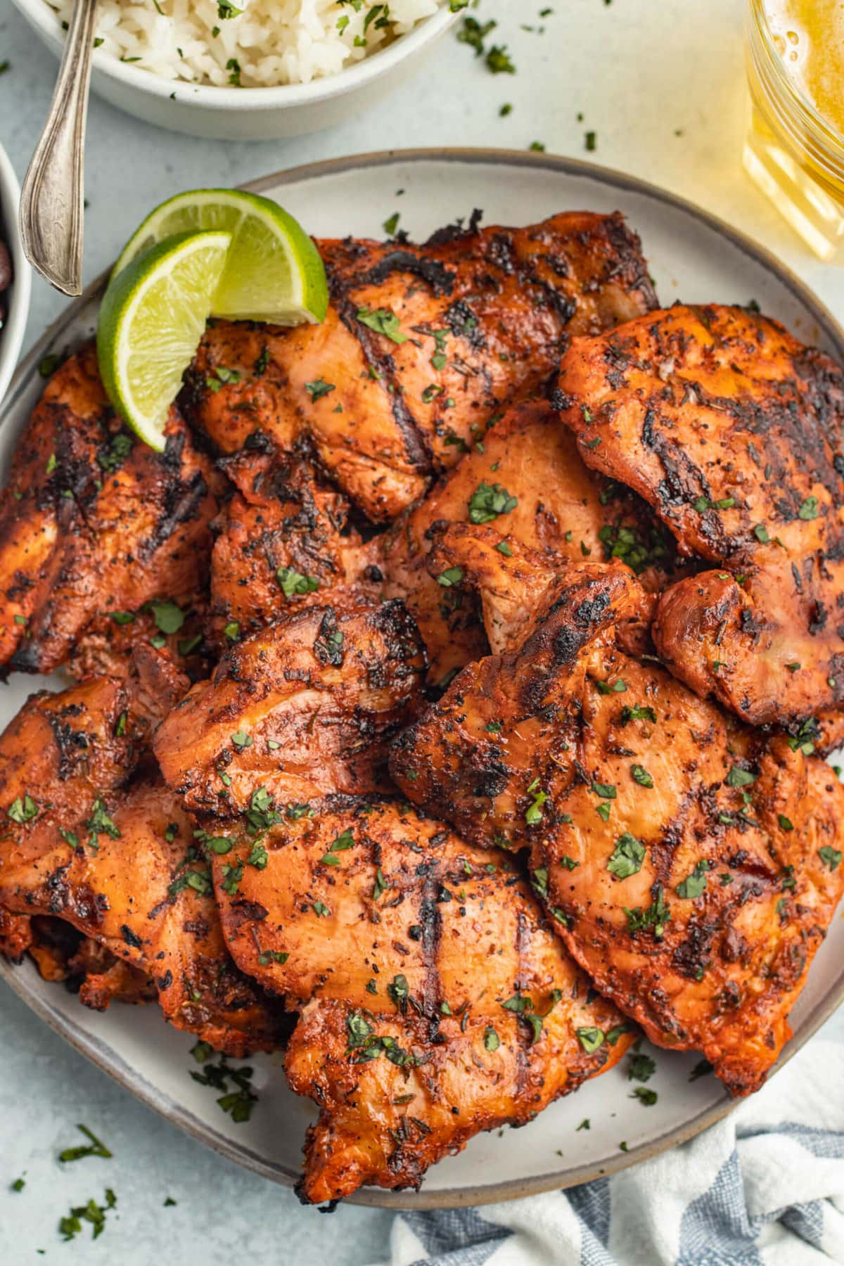 Grilled achiote chicken piled on a large round plate with a lime wedge.