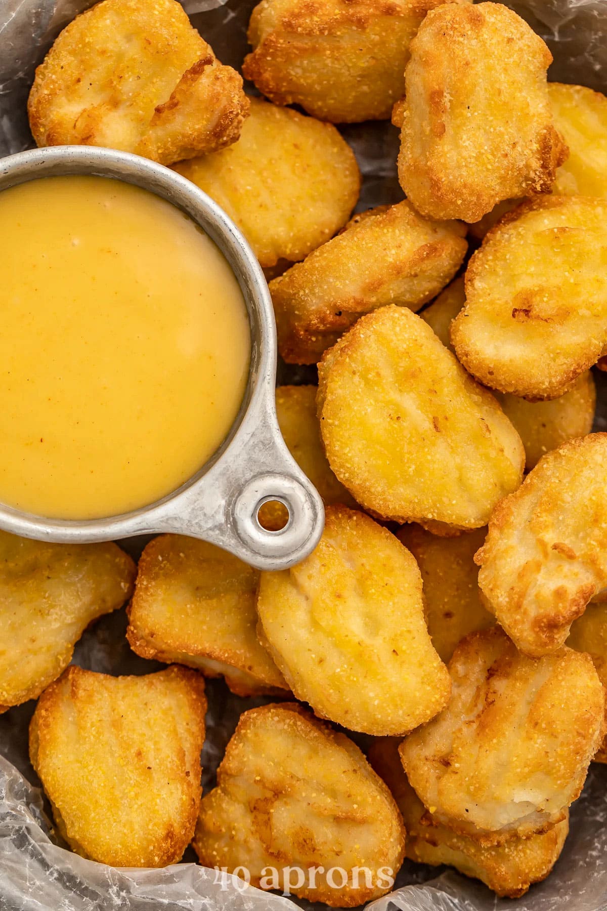 A pile of crispy air fryer chicken nuggets next to a small ramekin of honey mustard.