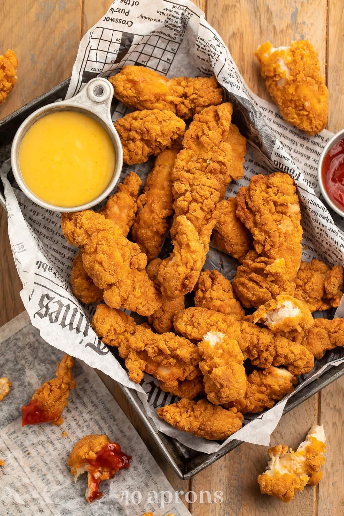 A pan lined with newsprint holding air fryer cooked chicken tenders and a small ramekin of honey mustard sauce.