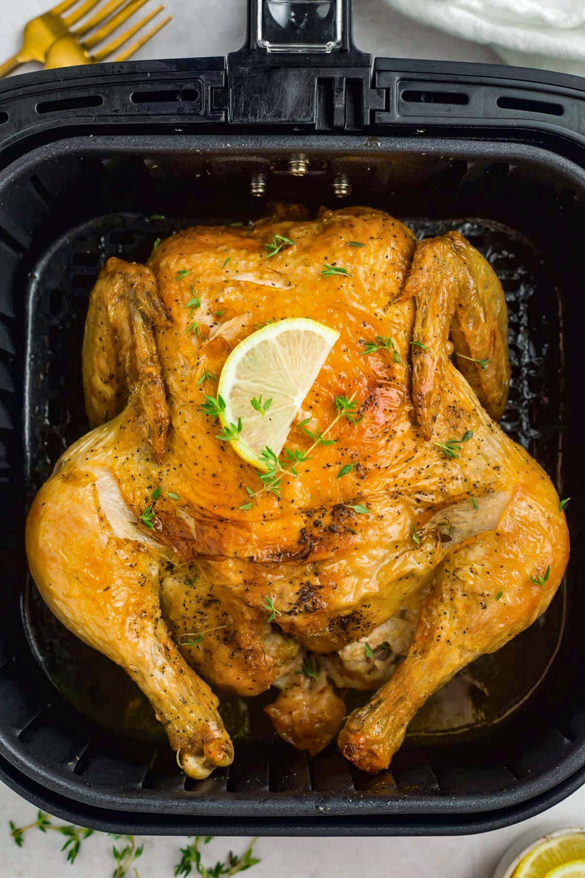 Overhead view of a golden, herb-rubbed whole chicken cooked in an air fryer then topped with a lemon wedge.