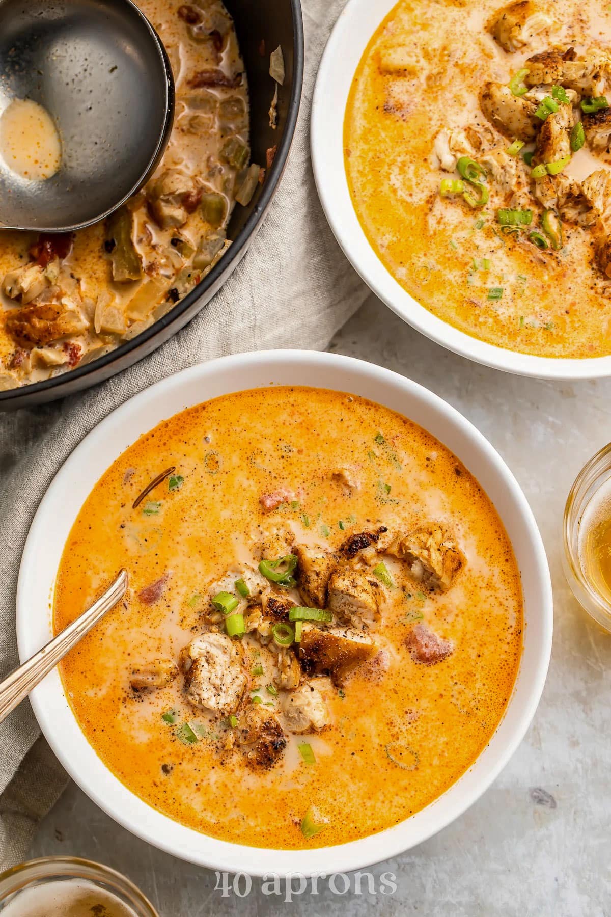 Top-down view of two bowls of deep orange, creamy, cajun chicken soup on a light grey table.