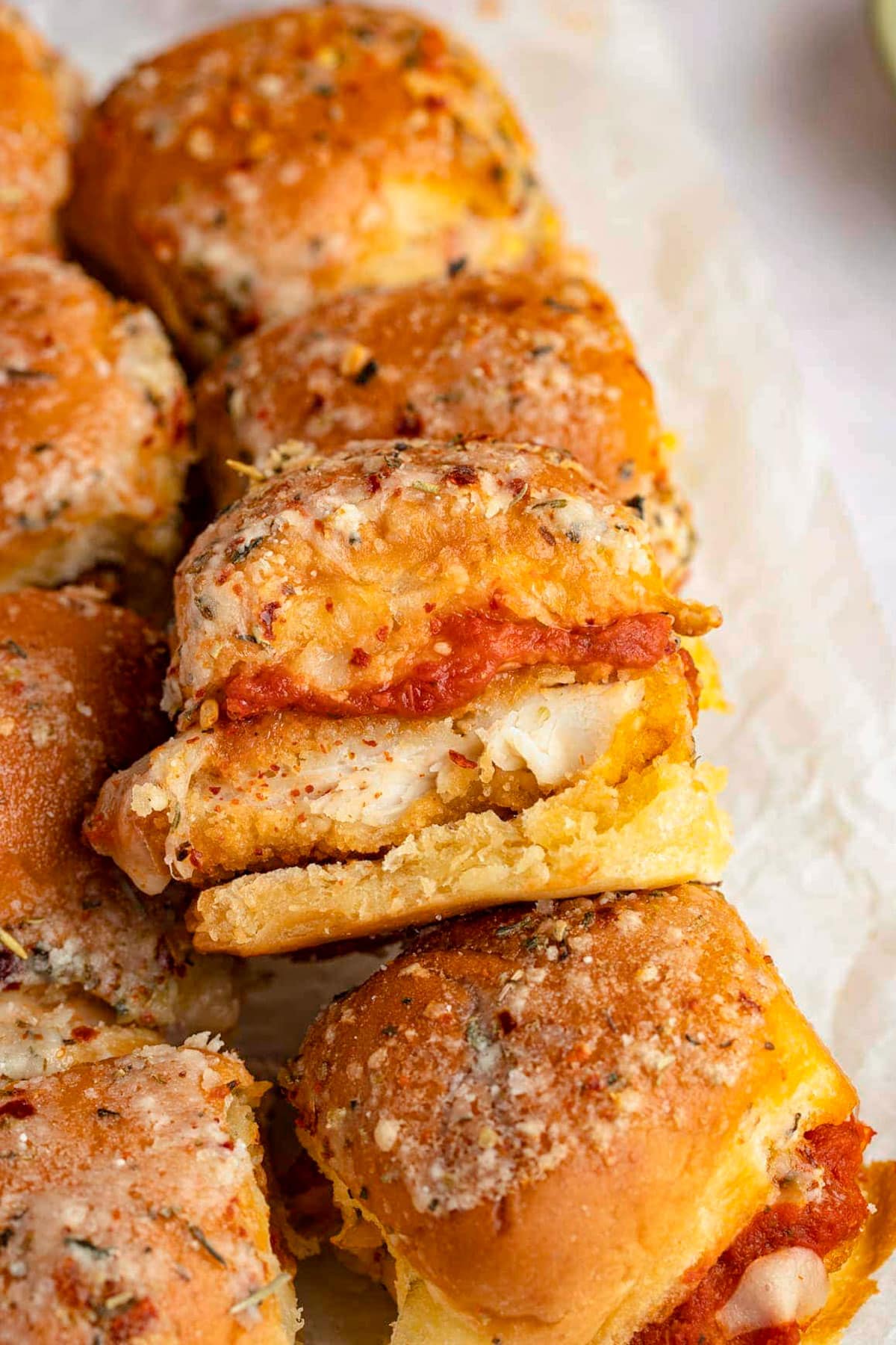 A tray of crispy chicken parm sliders, with one slider propped up on top of another to show the chicken inside.