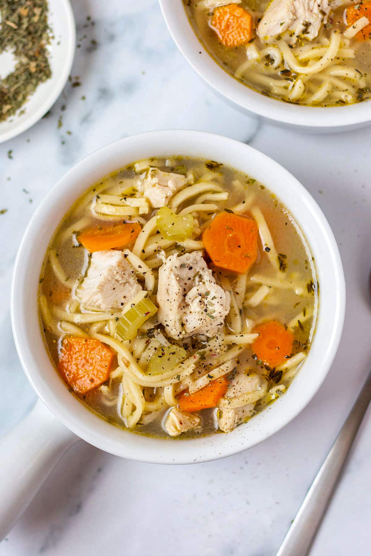 A small white soup bowl of chunky chicken noodle soup on a white tabletop.