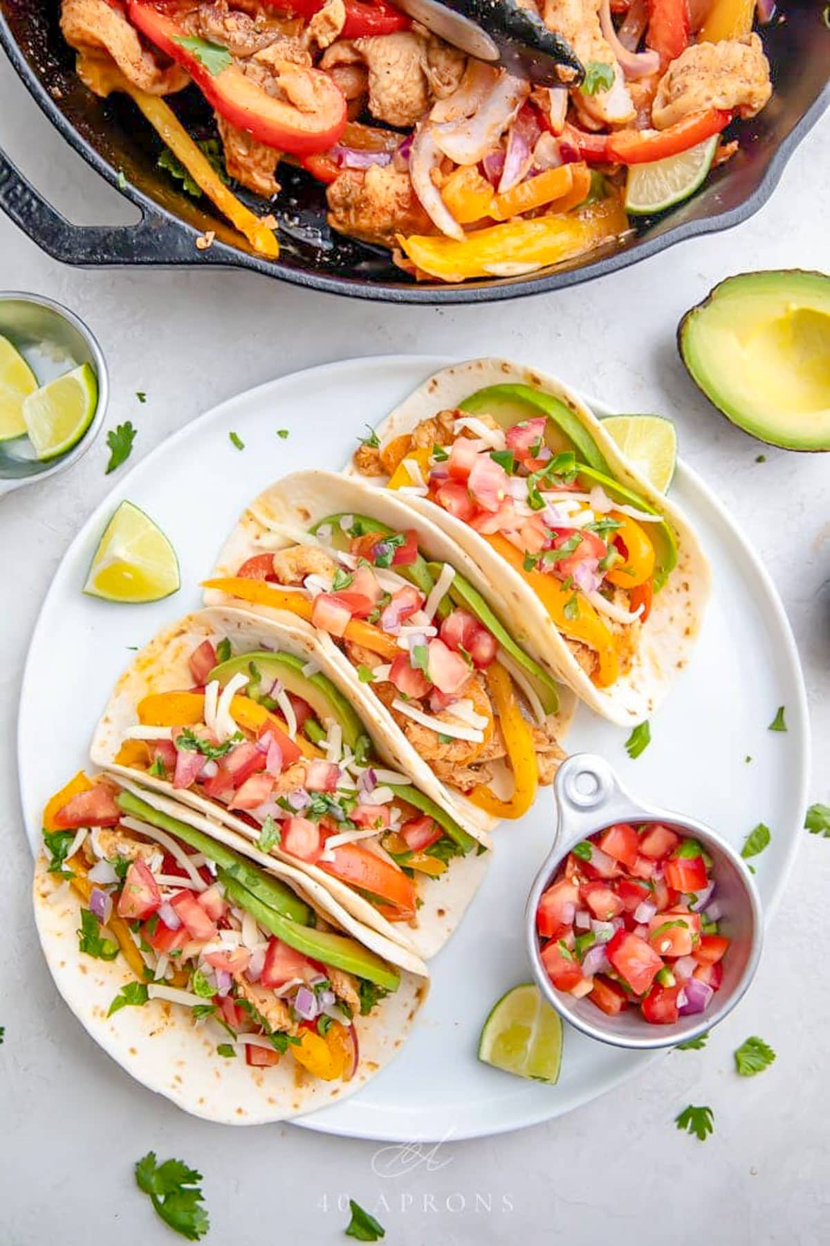 Crockpot chicken fajitas, with 4 fajitas in flour tortillas lined up on a white plate with a small ramekin of pico de gallo.