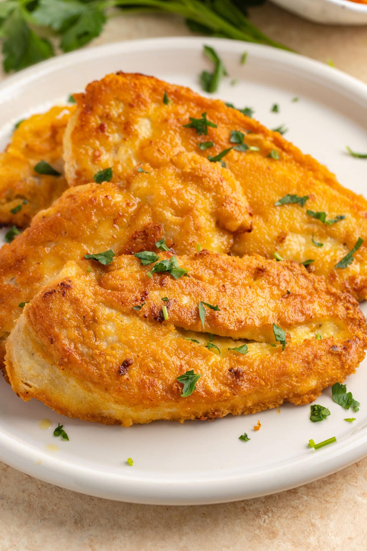 Three crusted chicken romano on a plate with a sprinkle of green fresh herbs.