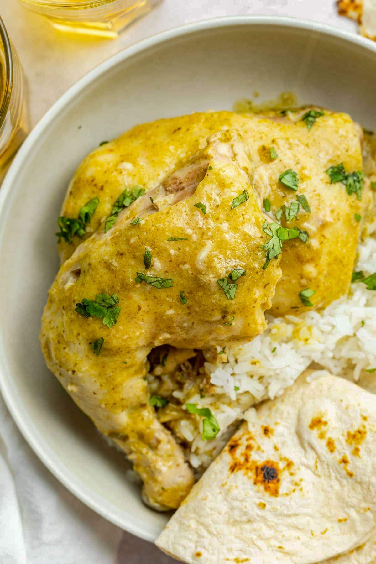 Bone-in chicken smothered in a green molé sauce and plated with rice and a tortilla triangle in a large bowl.