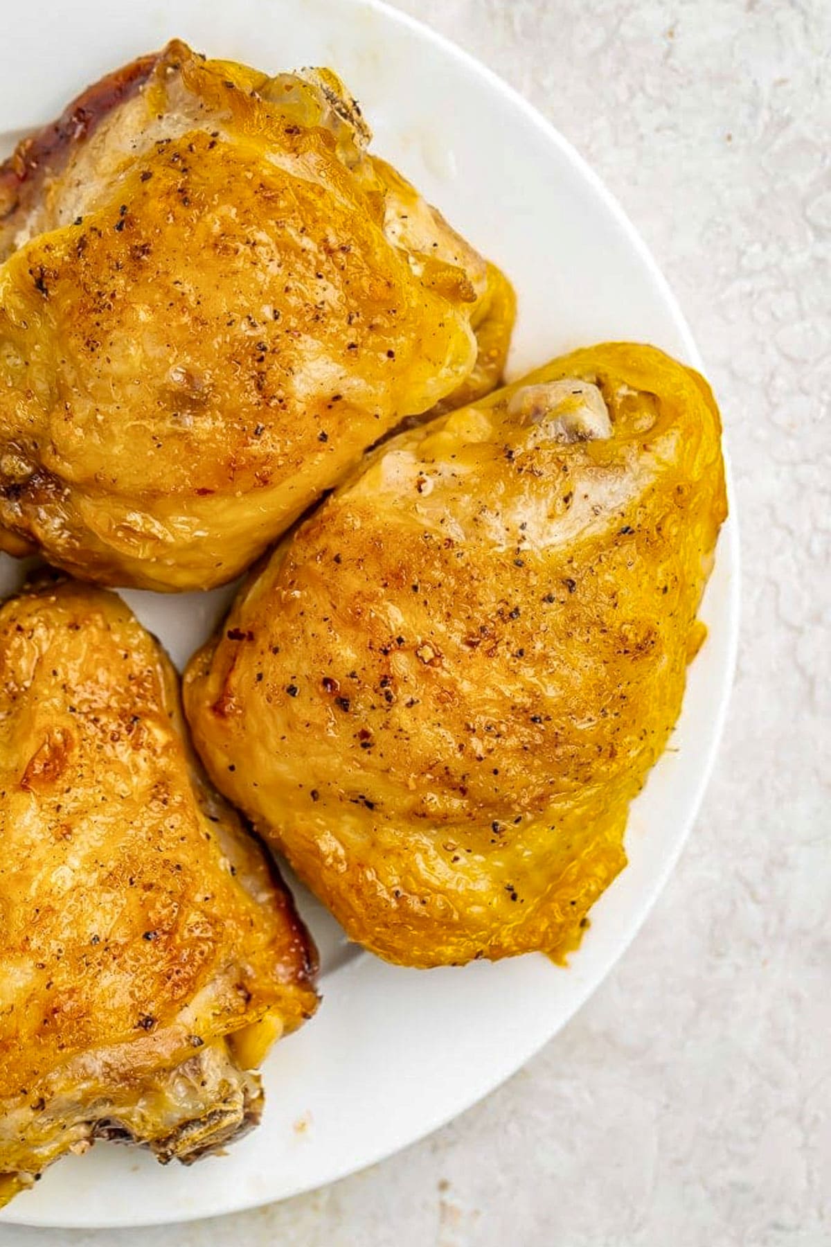 Previously-frozen chicken thighs, seasoned and then cooked in the Instant Pot, placed on a small white plate on a neutral tabletop.