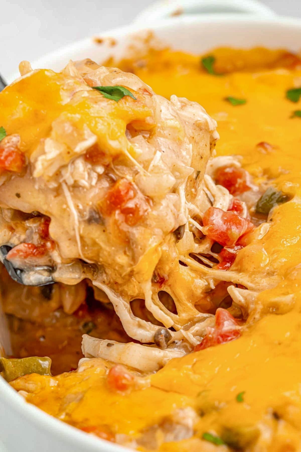 A large scoop of cheesy chicken king ranch casserole being lifted out of a casserole dish with a large spoon.