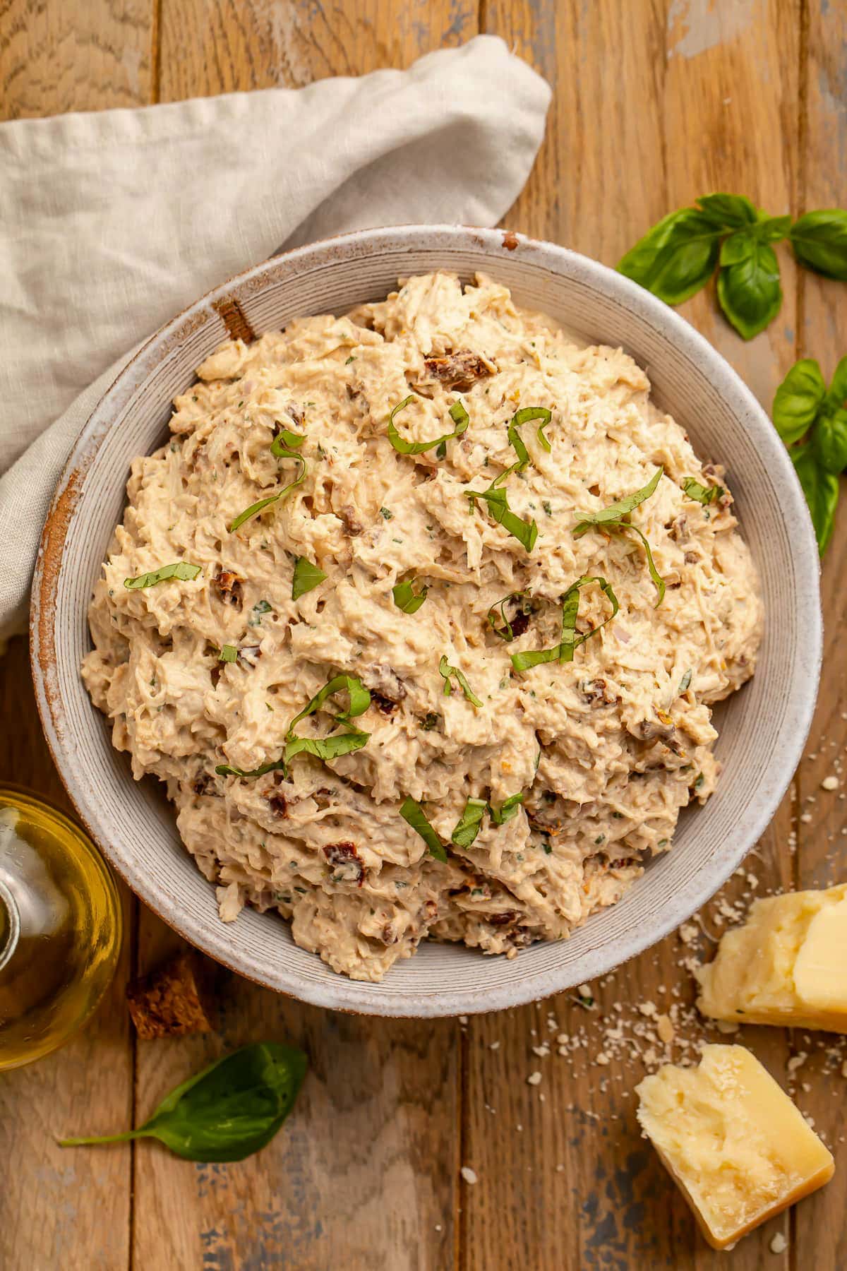 A large bowl holding creamy marry me chicken salad with shredded chicken, sun-dried tomatoes, and fresh basil on a wooden table.