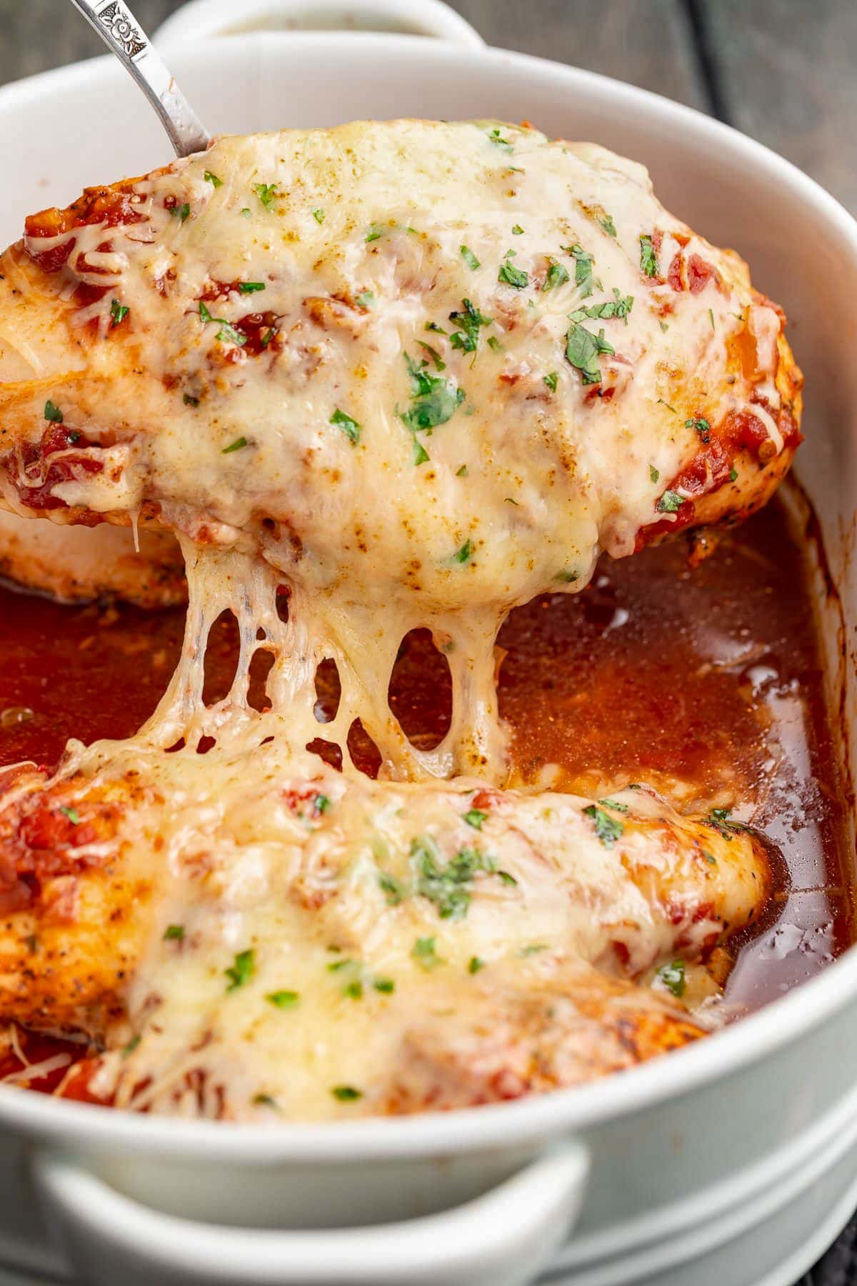 A cheesy salsa chicken breast being lifted out of a casserole dish.