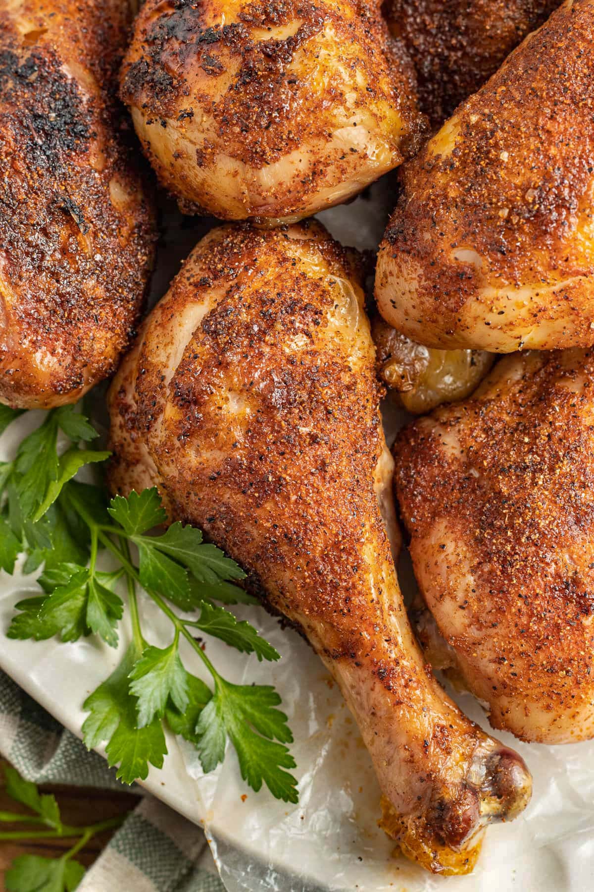 Smoked, dry rubbed chicken legs on a platter garnished with fresh greens.