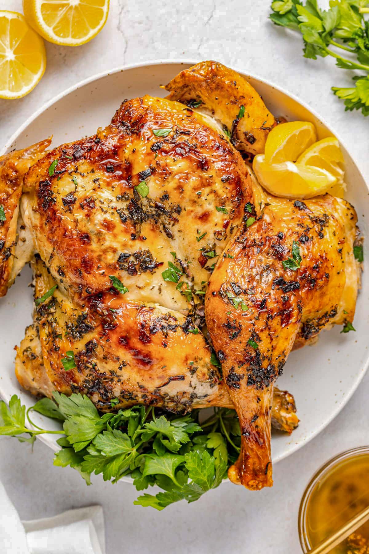 A whole spatchcocked chicken rubbed with garlic herb butter, roasted, and plated on a platter with green ganrish.