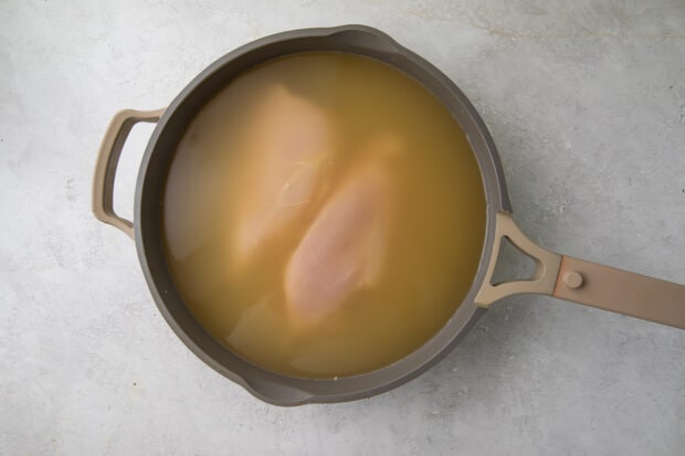 Raw chicken breasts in skillet of water