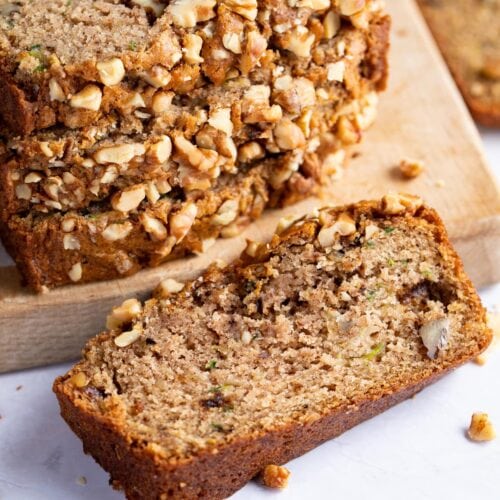 A single slice of vegan zucchini bread in front of a stack of other slices, on light surface